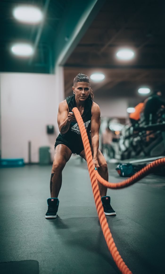 Services Athletic person performing an intense battle rope exercise in a modern gym setting.