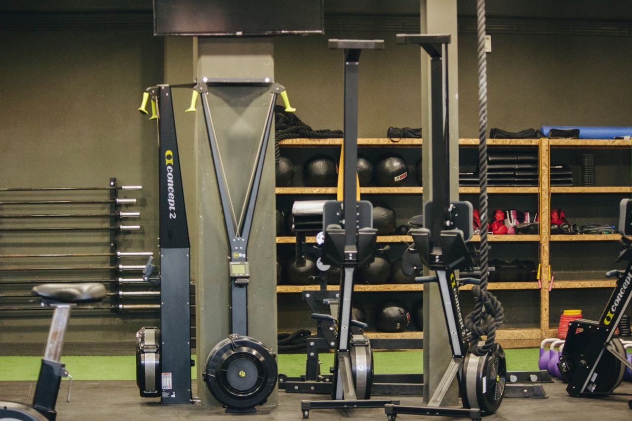 Services Modern gym with exercise equipment including rowing and ski machines, weights, and ropes.
